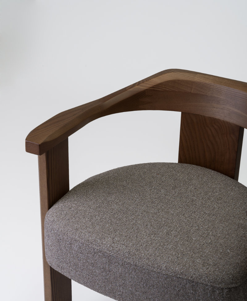 Image of the Nebula chair showcasing its embracing solid wood backrest from a three-quarter angle.