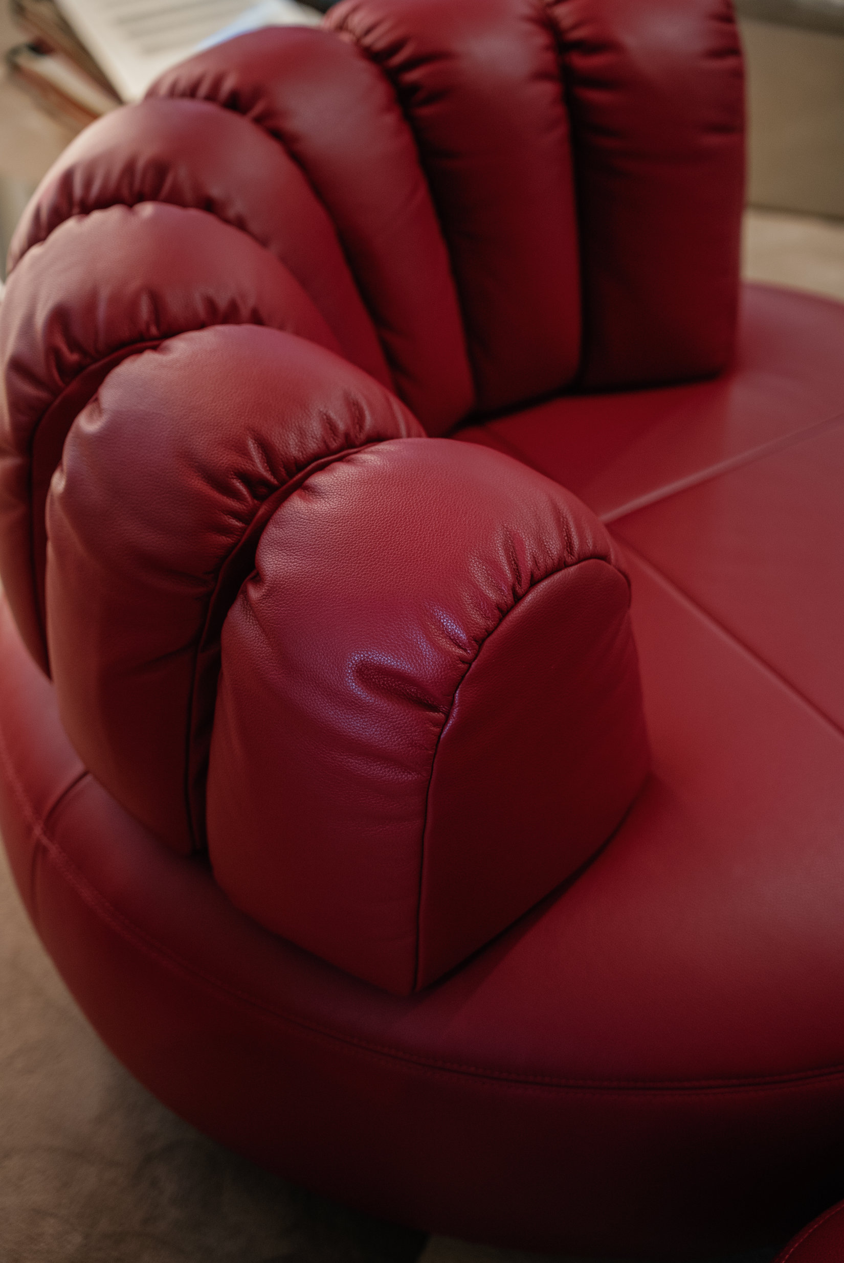 Upholstered lounge chair with circular base and segmented padded backrest, soft sculptural design. during milan design week