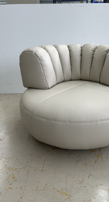 Upholstered lounge chair with circular base and segmented padded backrest, soft sculptural design.