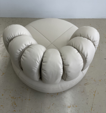 Upholstered lounge chair with circular base and segmented padded backrest, soft sculptural design.