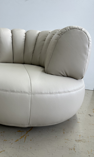 Upholstered lounge chair with circular base and segmented padded backrest, soft sculptural design.